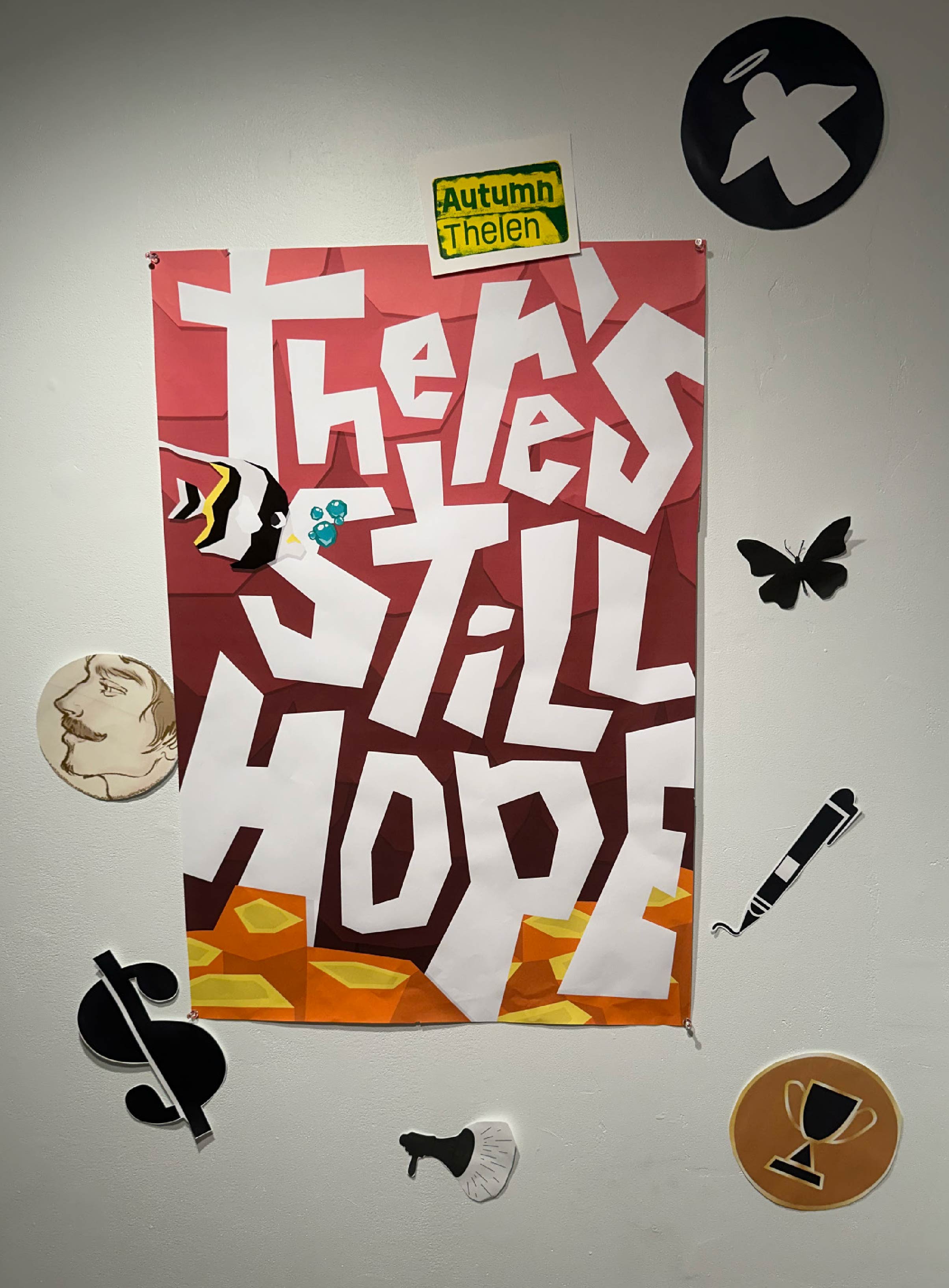 a poster that reads 'there's still hope' with a fish and coral nearby hangs on the wall surrounded by icons of other participants of the art exhibition